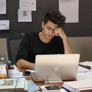 Student writing thesis at desk with books and laptop.