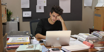 Student writing thesis at desk with books and laptop.