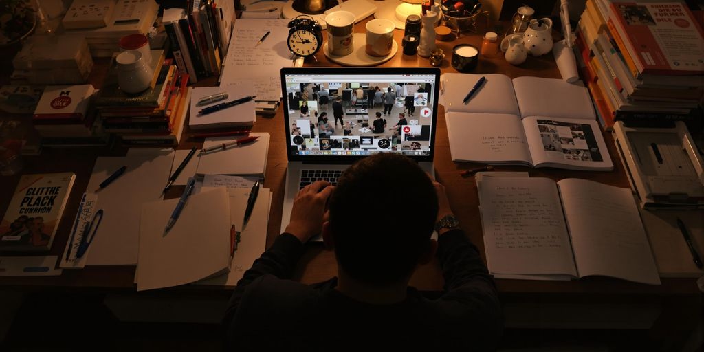 A person writing at a desk with books and a laptop.