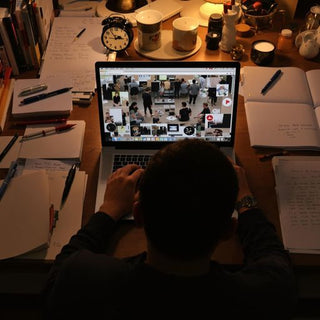 A person writing at a desk with books and a laptop.