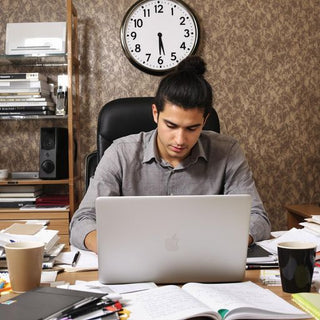 Student writing thesis at a busy desk with books.