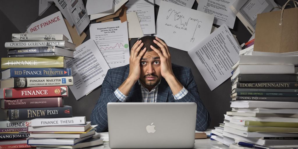 Student stressed over finance thesis with books and laptop.