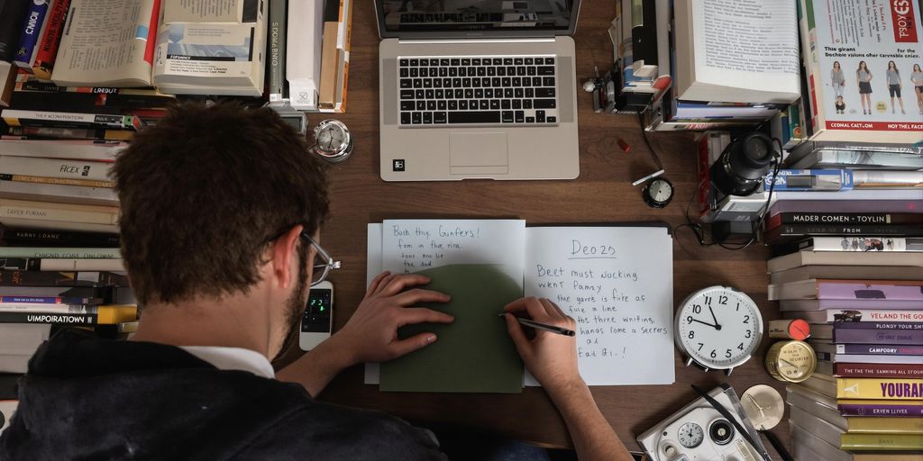 Student writing thesis at desk with books and laptop.