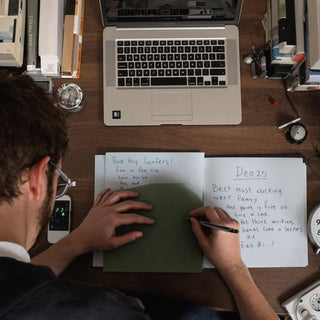 Student writing thesis at desk with books and laptop.