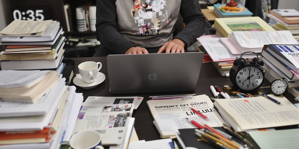 Person writing thesis at a cluttered desk.