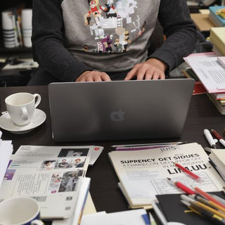 Person writing thesis at a cluttered desk.