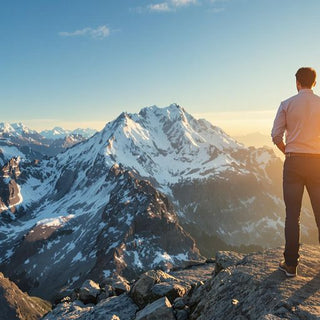 Business professional on a mountain peak under a bright sky.