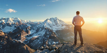 Business professional on a mountain peak under a bright sky.