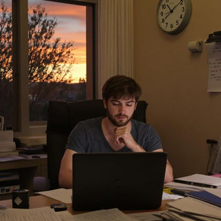 Student writing thesis at desk with books and laptop.