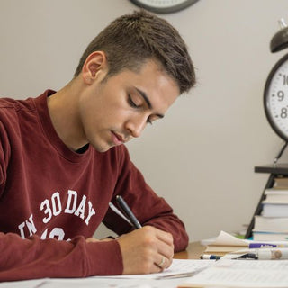 Student writing with books and a clock nearby.