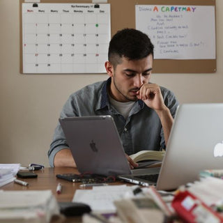 Student writing thesis at desk with books and laptop.