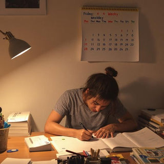 Person writing at a desk with books and notes.