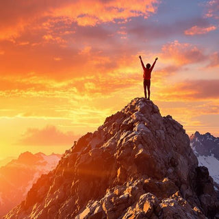 Person on mountain peak celebrating success at sunrise.