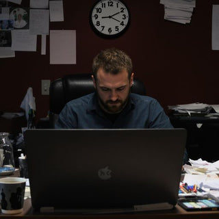 Person writing at a desk with coffee cups and papers.