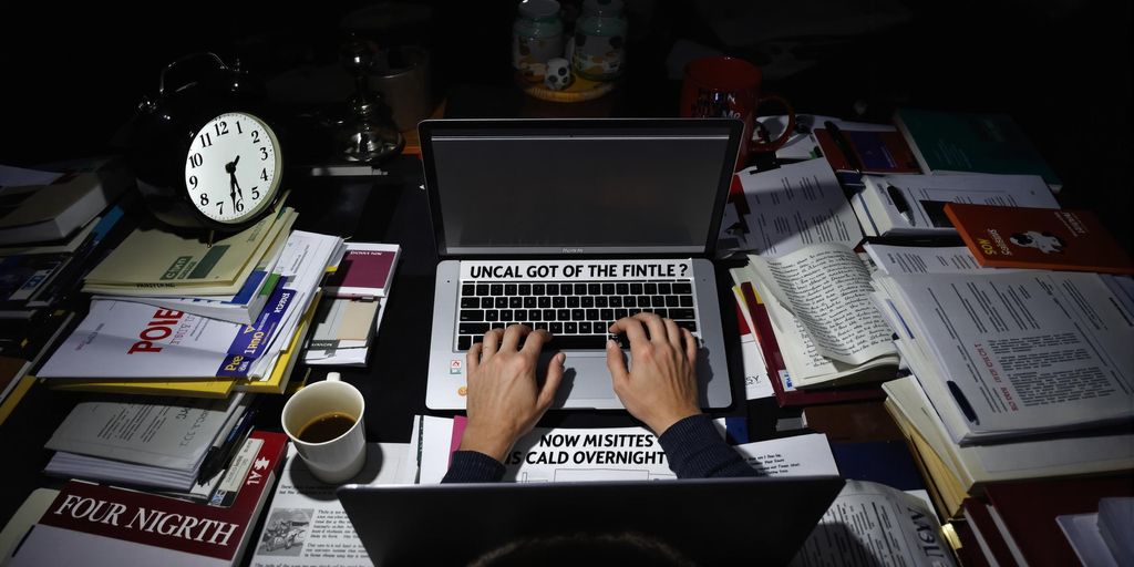 Person writing thesis at night with coffee and books.