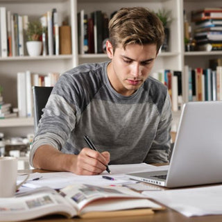 Student writing thesis at a desk with books.