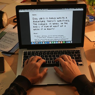 Person writing at a desk with a laptop and coffee.