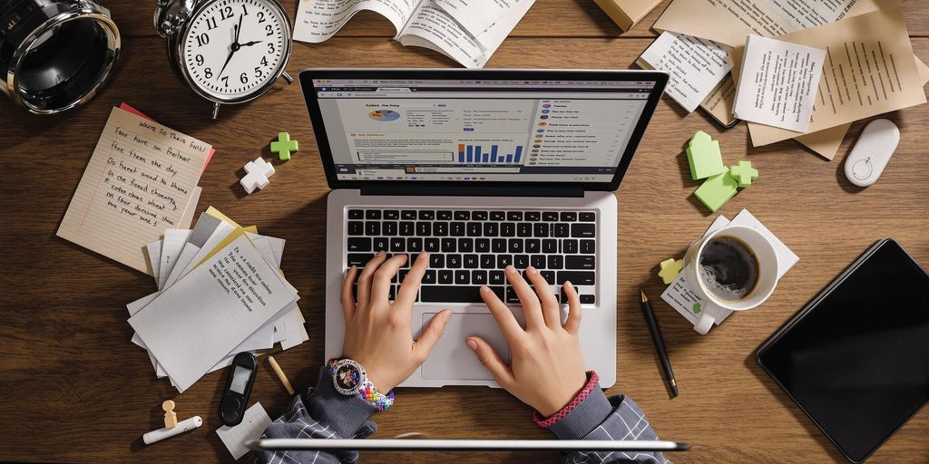 Student typing rapidly on laptop amidst scattered notes.