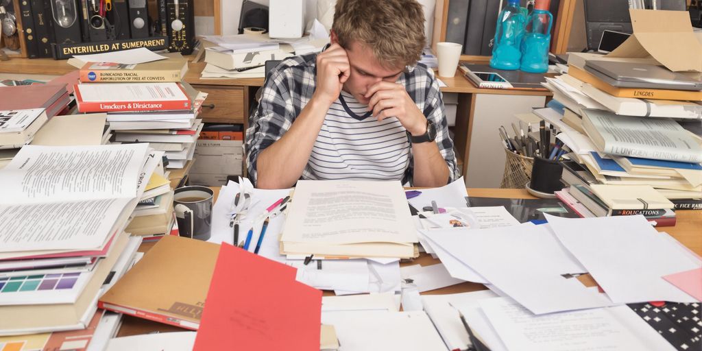 Student writing thesis at a cluttered desk.