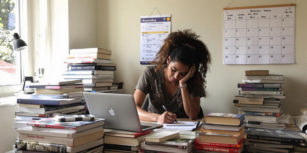 Student writing at a desk with books and laptop.