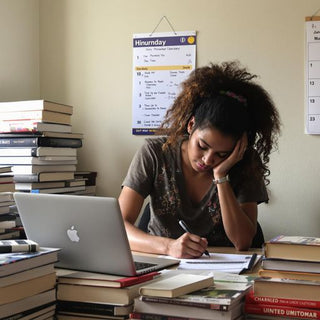 Student writing at a desk with books and laptop.