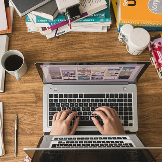 Person writing on laptop with books and coffee nearby.