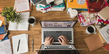 Person writing on laptop with books and coffee nearby.