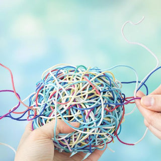 Hands untangling a colorful ball of yarn.