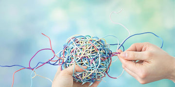Hands untangling a colorful ball of yarn.