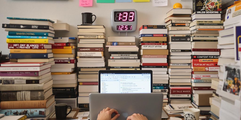 Person writing thesis with books and laptop in chaos.