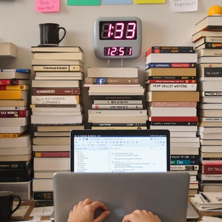 Person writing thesis with books and laptop in chaos.